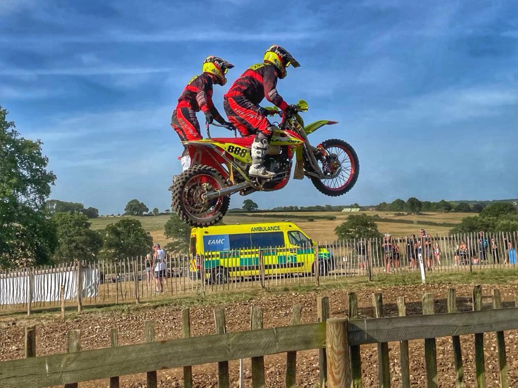 An EAMC emergency ambulance providing event medical cover and first aid at a motocross event with a sidecar motorbike mid jump