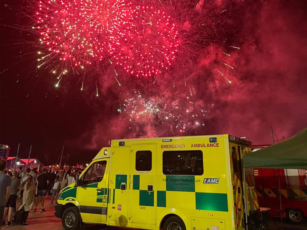 An EAMC emergency ambulance providing event medical and first aid cover at a firework event with fireworks exploding in the background